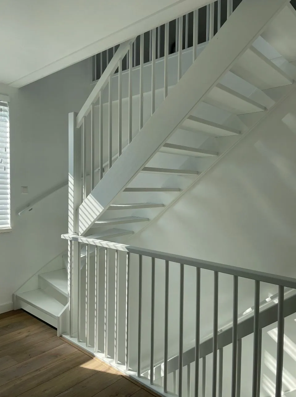 Wit geschilderde open trap met spijlen en balustrade
